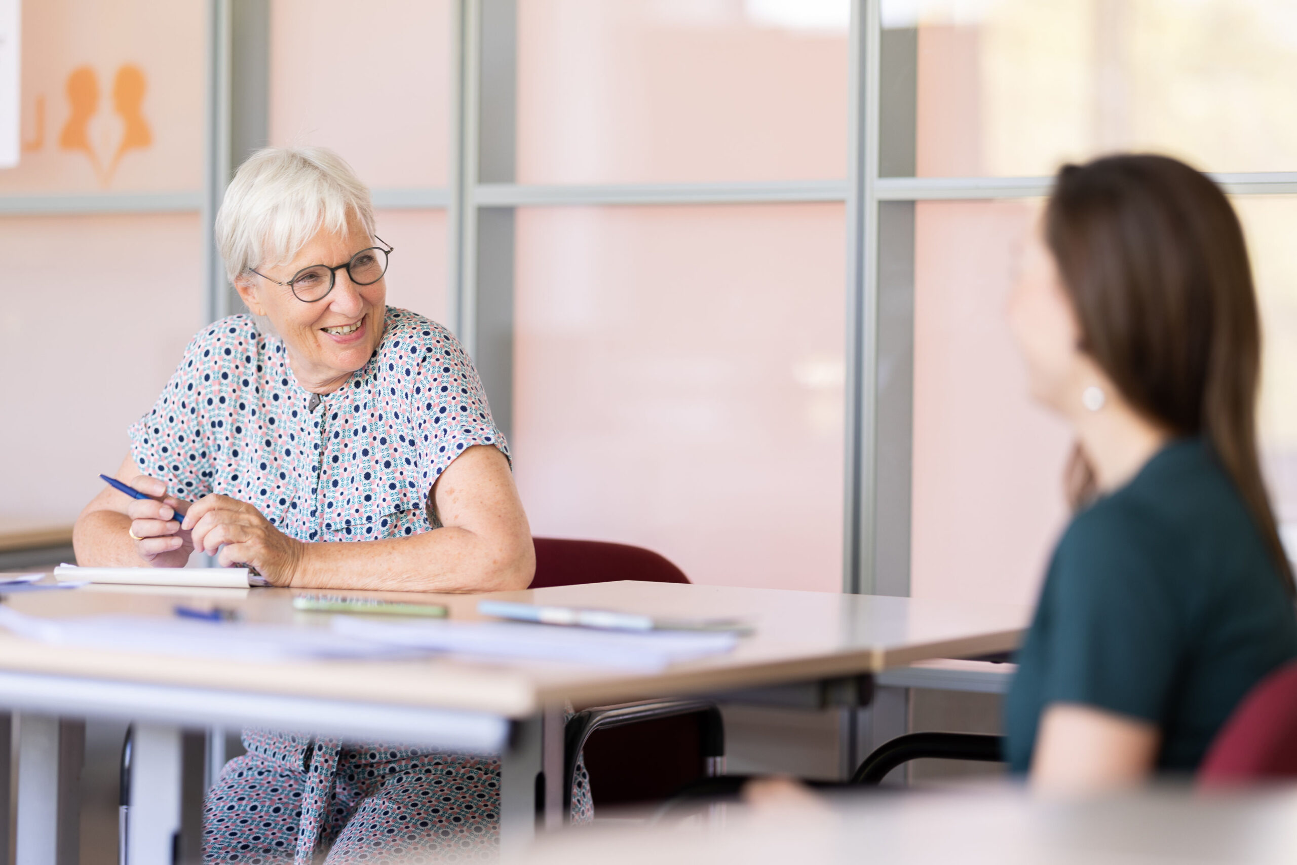 Docent en cursist in gesprek tijdens individuele Nederlandse les in een lichte lesruimte.