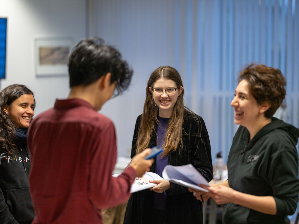 Cursisten werken in groepjes tijdens de Nederlandse les, onder begeleiding van een docent.