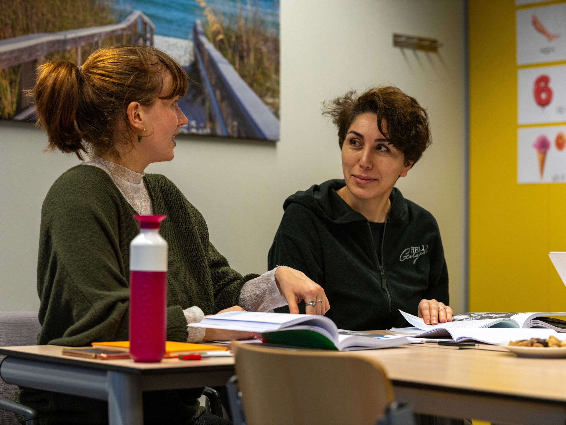 Twee cursisten in gesprek met open lesboeken op tafel bij de cursus Nederlands spreken in de praktijk B2.2.