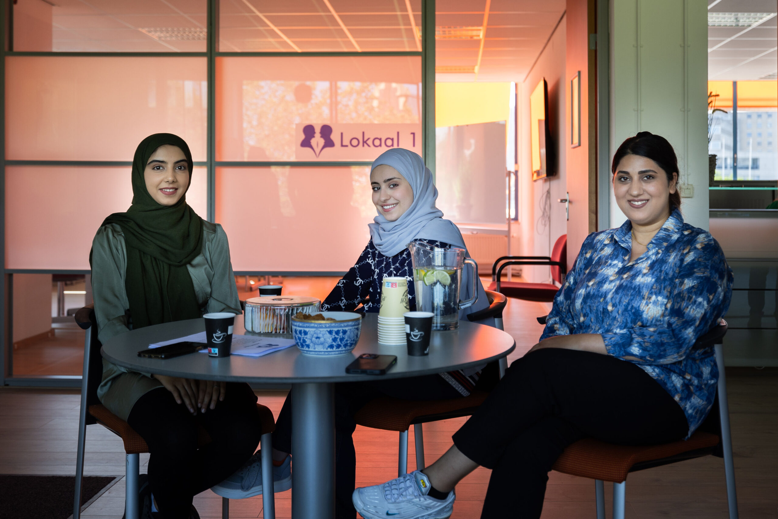 Drie jonge vrouwen zitten aan tafel in Lokaal 1 bij Lest Best, klaar voor de cursus Nederlands op A1-niveau.