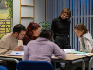 Een groep cursisten werkt geconcentreerd aan een opdracht in de klas, terwijl een docent hen ondersteunt.