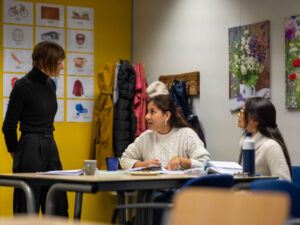Twee cursisten in gesprek met hun docent tijdens de les Nederlands, met lesmateriaal op tafel.