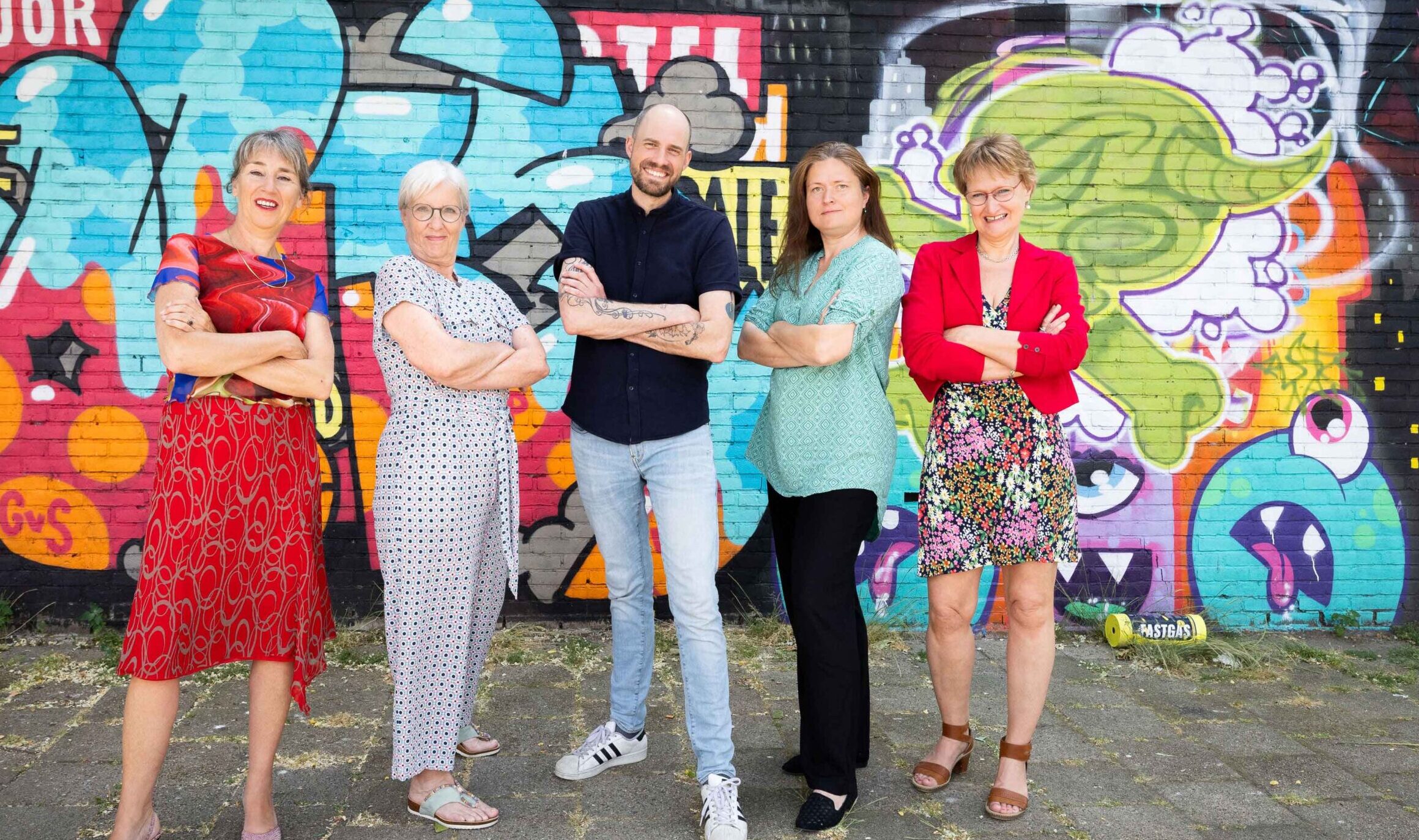 Teamleden van Lest Best poseren zelfverzekerd voor een kleurrijke graffitiwand in Rotterdam.